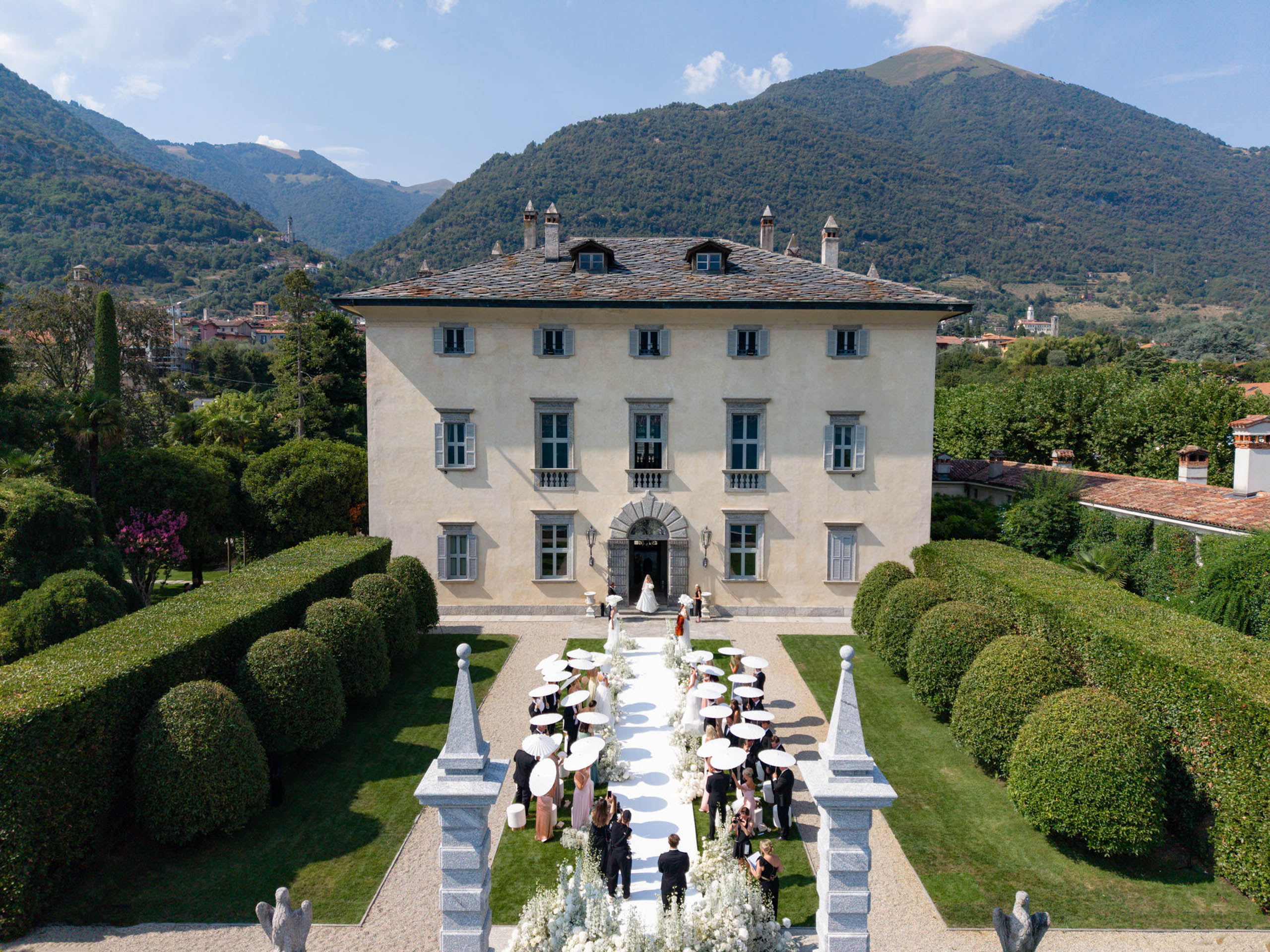 Eine Hochzeit im Freien in einer prächtigen Villa wie der Villa Balbiano, bei der die Gäste im Garten sitzen und im Hintergrund die Berge zu sehen sind – eine bezaubernde Kulisse für alle, die davon träumen, am Comer See zu heiraten.