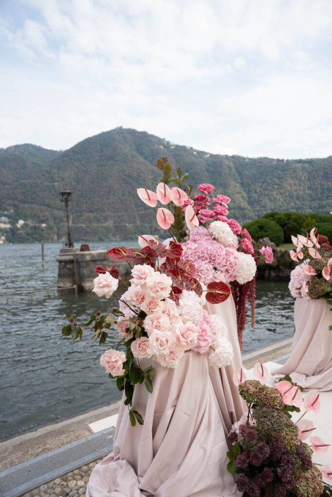 Rosa-weiße Blumenarrangements am Seeufer vor Bergkulisse – ein automatischer Entwurf natürlicher Schönheit.