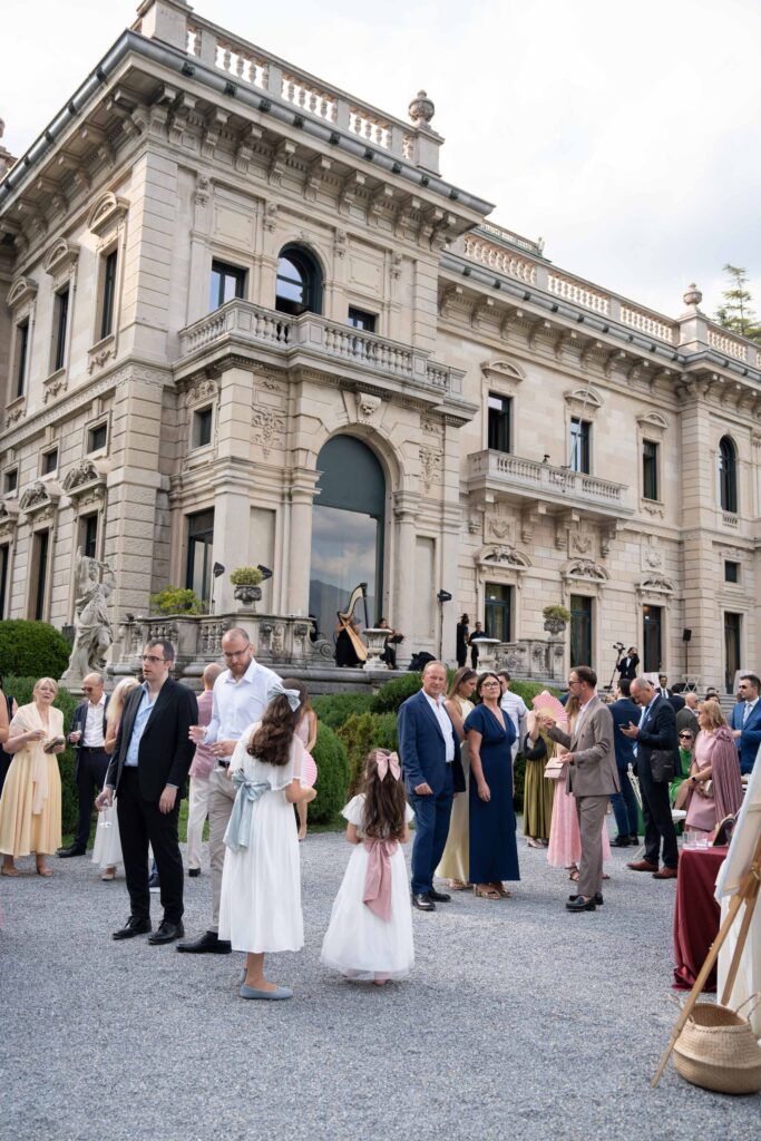 Menschen in festlicher Kleidung versammeln sich vor einem prächtigen Steingebäude zu einer Veranstaltung oder Feier im Rahmen von Automatischer Entwurf.