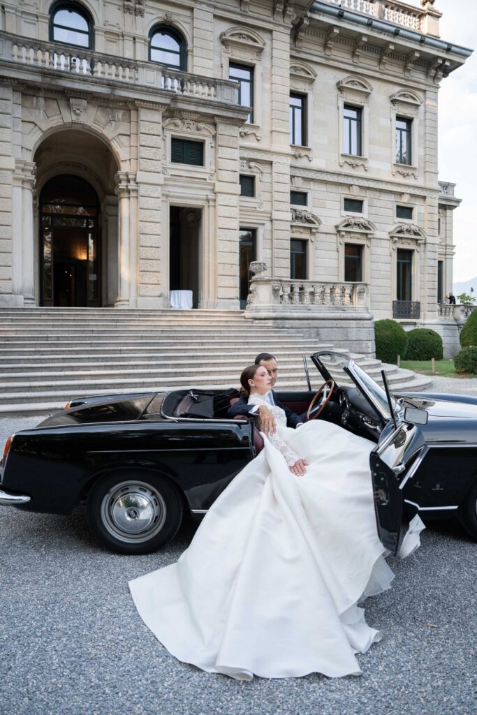 The bride and groom pose next to a black convertible in front of a magnificent historical building – automatic design.
