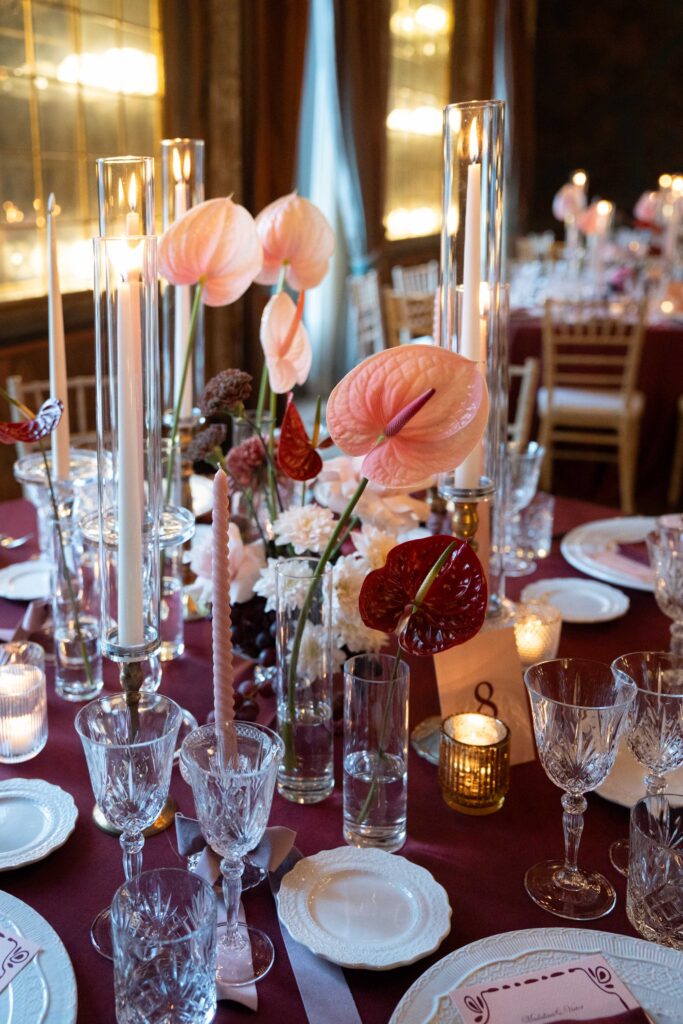 Elegante Tischdekoration mit rosa Blumen, Kerzen und Gläsern auf einer burgunderroten Tischdecke – automatischer Entwurf.
