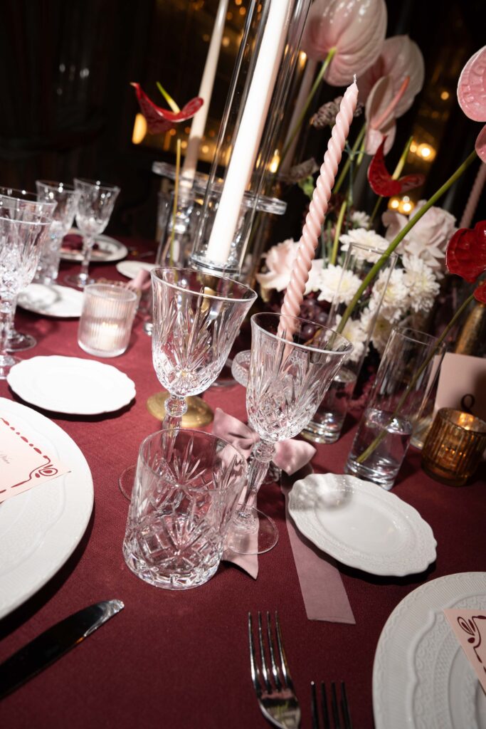 Elegante Tischdekoration mit Kristallgläsern, rosa Kerzen und einem roten Blumengesteck als automatischer Entwurf.