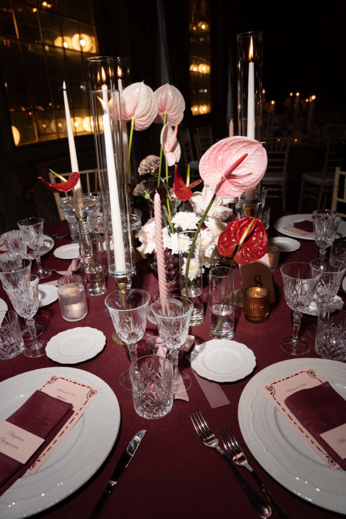 Elegante Tischdekoration mit rosa und roten Blumen, Kerzen und einer automatischen Anordnung burgunderroter Servietten.