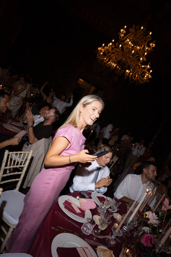 Eine Frau in einem rosa Kleid lächelt bei einem festlichen Abendessen mit Automatischer Entwurf und eleganter Tischdekoration.