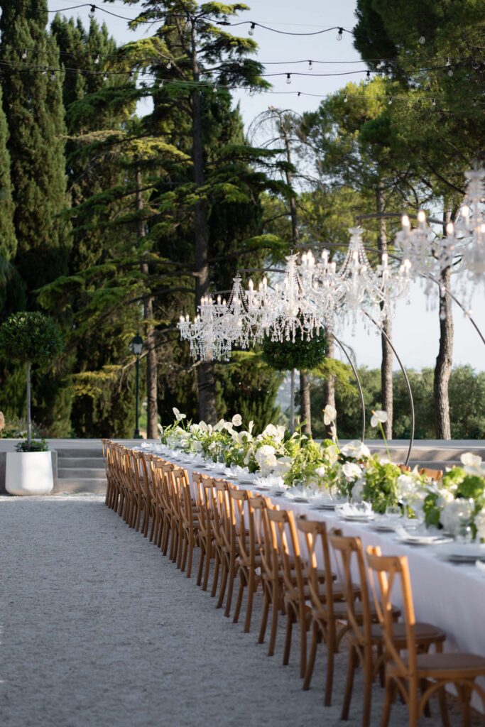 Hochzeit im Maniero Montecassiano: Euer Hochzeitswochenende in einer Boutique-Villa in den Marken 26 Ein langer Banketttisch im Freien im Maniero Montecassiano, gedeckt für eine feierliche Veranstaltung unter Kronleuchtern.