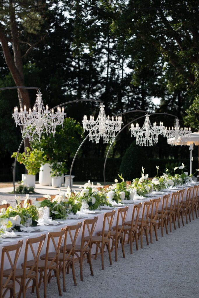 Hochzeit im Maniero Montecassiano: Euer Hochzeitswochenende in einer Boutique-Villa in den Marken 19 Ein langer Esstisch im Freien im Maniero Montecassiano, geschmückt mit weißen Blumen und Kristallkronleuchtern.