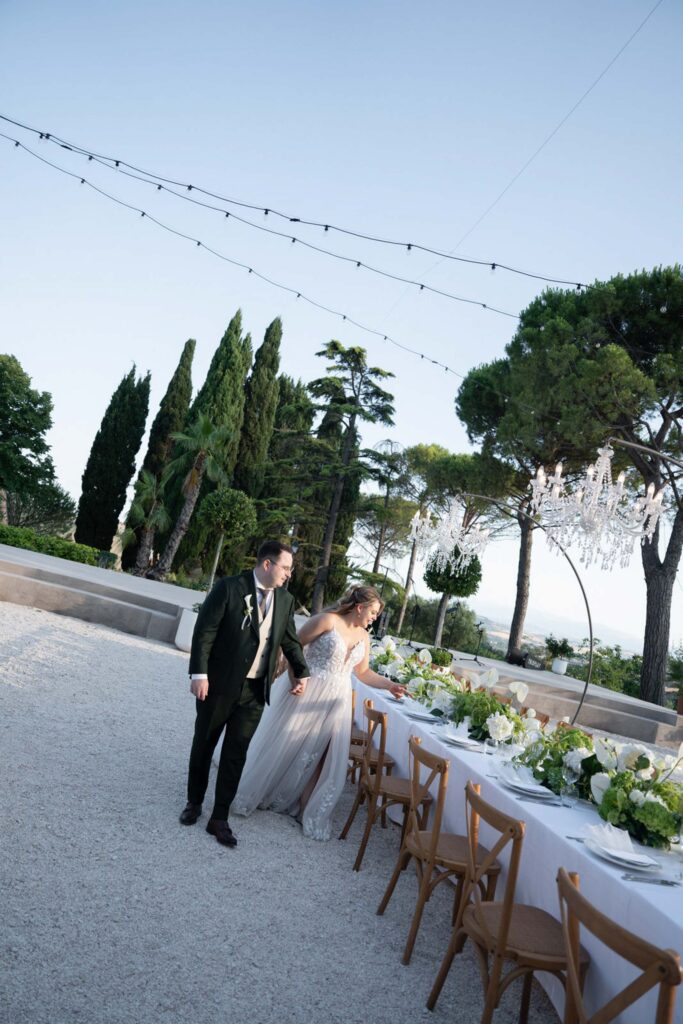 Hochzeit im Maniero Montecassiano: Euer Hochzeitswochenende in einer Boutique-Villa in den Marken 21 Ein Brautpaar geht Hand in Hand an einem geschmückten Hochzeitstisch im Maniero Montecassiano vorbei.