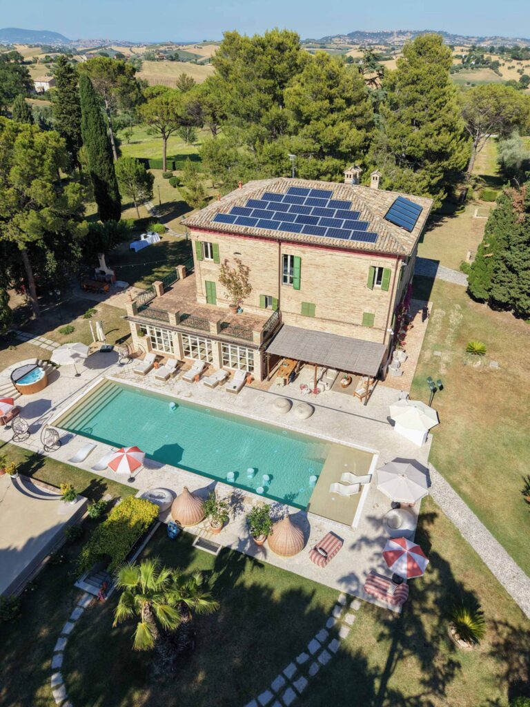 Hochzeit im Maniero Montecassiano: Euer Hochzeitswochenende in einer Boutique-Villa in den Marken 12 Luftaufnahme von Maniero Montecassiano, einer Backsteinvilla mit Sonnenkollektoren, einem Pool und Liegestühlen.