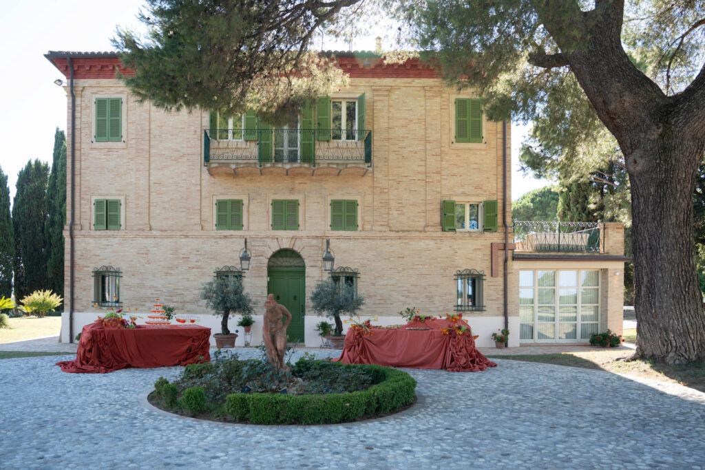 Hochzeit im Maniero Montecassiano: Euer Hochzeitswochenende in einer Boutique-Villa in den Marken 9 Die Villa Maniero Montecassiano mit zwei Tischen im Freien und einer Skulptur in der Mitte des Gartens.