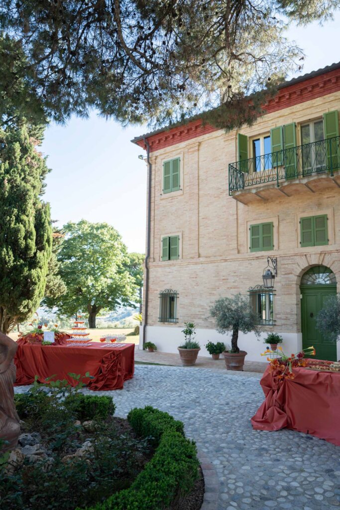 Hochzeit im Maniero Montecassiano: Euer Hochzeitswochenende in einer Boutique-Villa in den Marken 51 Tische mit roten Tischdecken, die für eine Veranstaltung im Freien vor der Villa Maniero Montecassiano aufgestellt wurden.