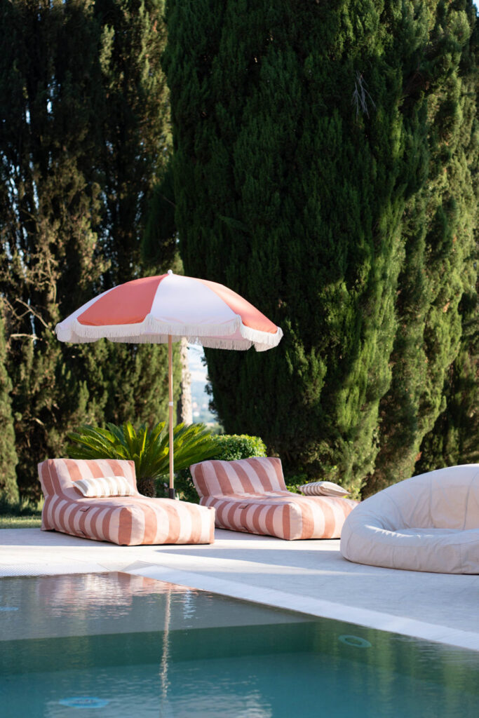 Hochzeit im Maniero Montecassiano: Euer Hochzeitswochenende in einer Boutique-Villa in den Marken 59 Zwei gestreifte Liegestühle unter einem rot-weißen Sonnenschirm am Pool des Maniero Montecassiano.
