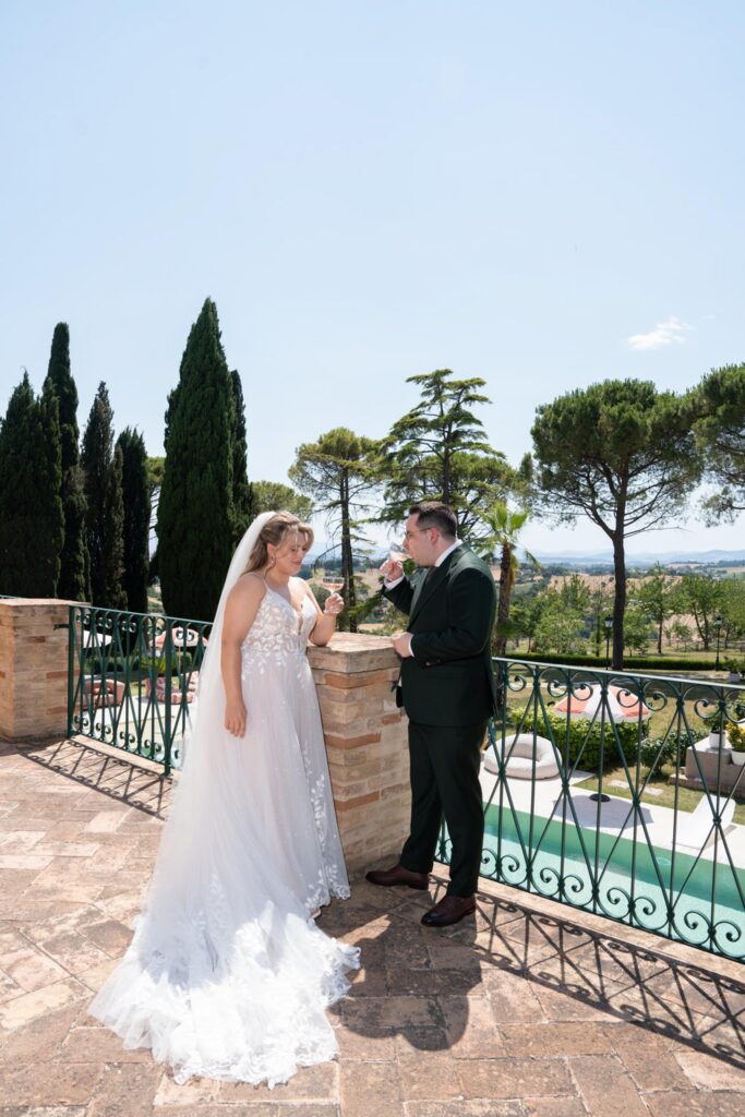 Hochzeit im Maniero Montecassiano: Euer Hochzeitswochenende in einer Boutique-Villa in den Marken 65 Ein Brautpaar stößt auf einer Steinterrasse bei einer Hochzeit im Maniero Montecassiano mit Gläsern an.
