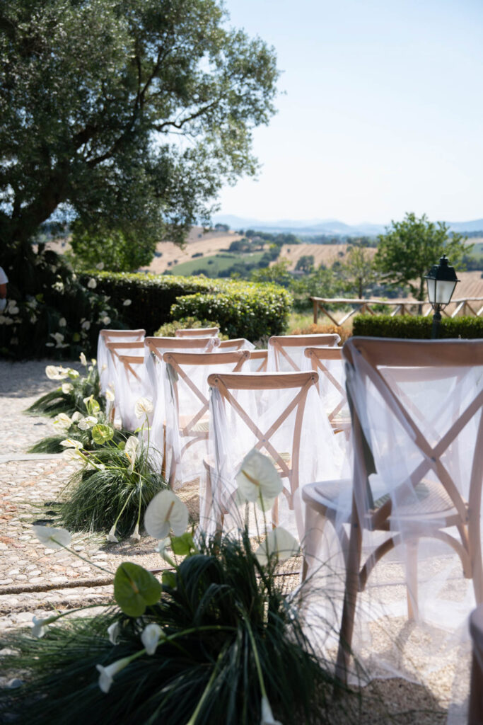 Hochzeit im Maniero Montecassiano: Euer Hochzeitswochenende in einer Boutique-Villa in den Marken 35 Holzstühle mit weißem Tüll säumen einen Gang im Freien bei einer Hochzeit in den Marken.