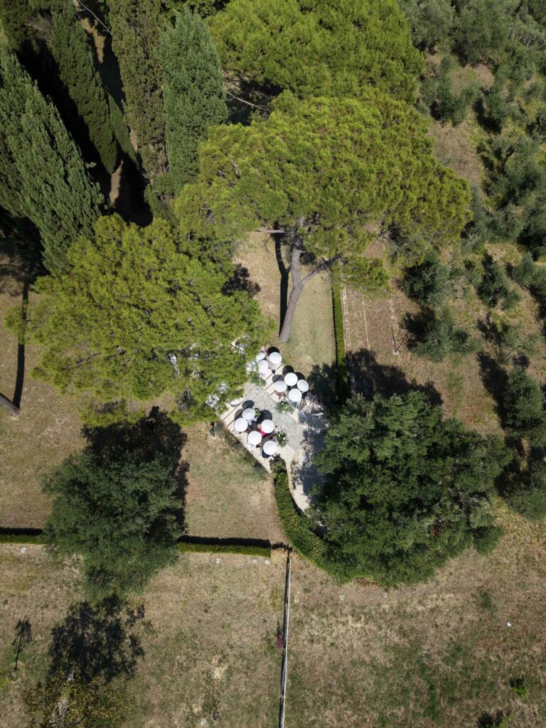 Hochzeit im Maniero Montecassiano: Euer Hochzeitswochenende in einer Boutique-Villa in den Marken 42 Luftaufnahme von Tischen im Freien, die unter großen Bäumen für eine Hochzeit in den Marken aufgestellt wurden.