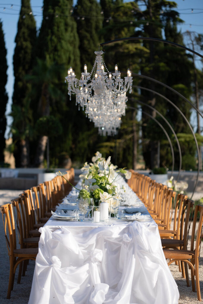 Hochzeit im Maniero Montecassiano: Euer Hochzeitswochenende in einer Boutique-Villa in den Marken 22 Ein langer Hochzeitstisch im Freien im Maniero Montecassiano, über dem ein Kristallleuchter hängt.