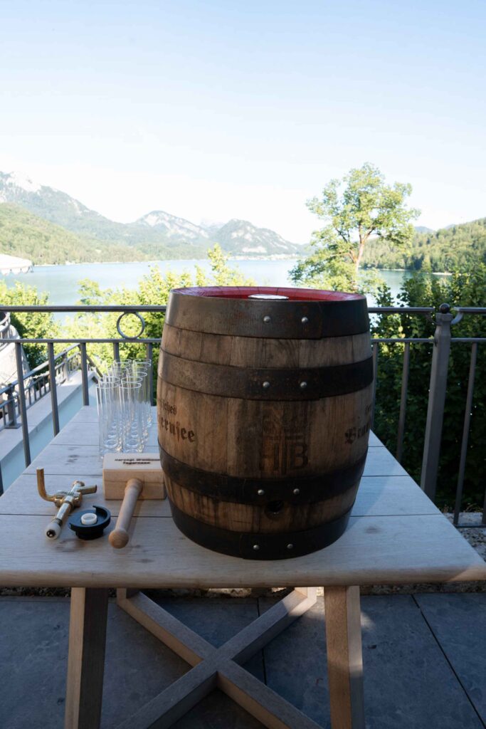 Ein Bierfass aus Holz, ein Zapfhahn und Gläser in der Lage am See des Rosewood Schloss Fuschl.