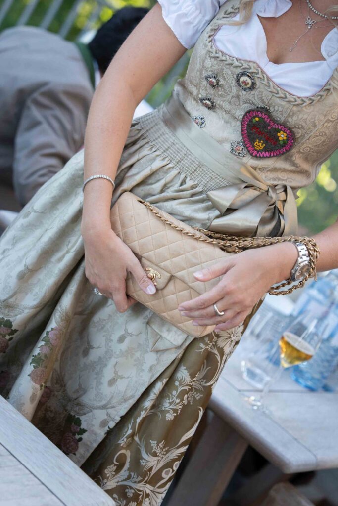 Eine Frau in einem traditionellen Dirndl hält im Rosewood Schloss Fuschl eine beigefarbene Chanel-Handtasche in der Hand.