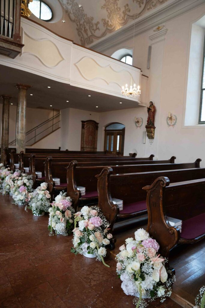 Kirchenbänke, geschmückt mit Blumengestecken für eine Hochzeit auf Schloss Fuschl.