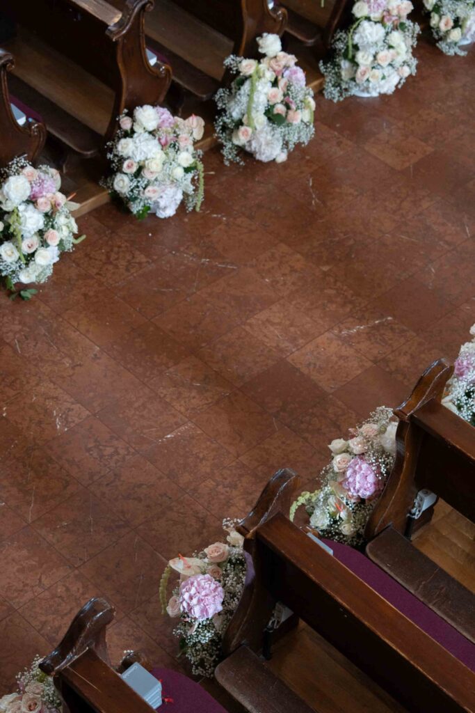 Blumenschmuck auf den Kirchenbänken entlang des Mittelgangs bei einer Hochzeit auf Schloss Fuschl.