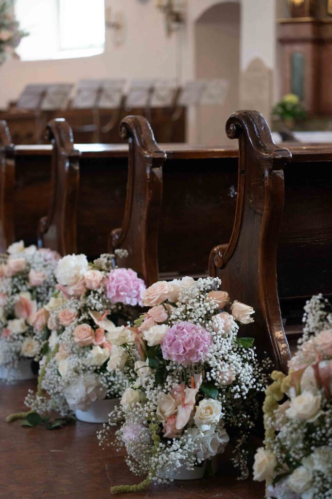 Blumenarrangements aus Rosen und Hortensien schmücken die Holzbänke bei einer Hochzeit auf Schloss Fuschl.