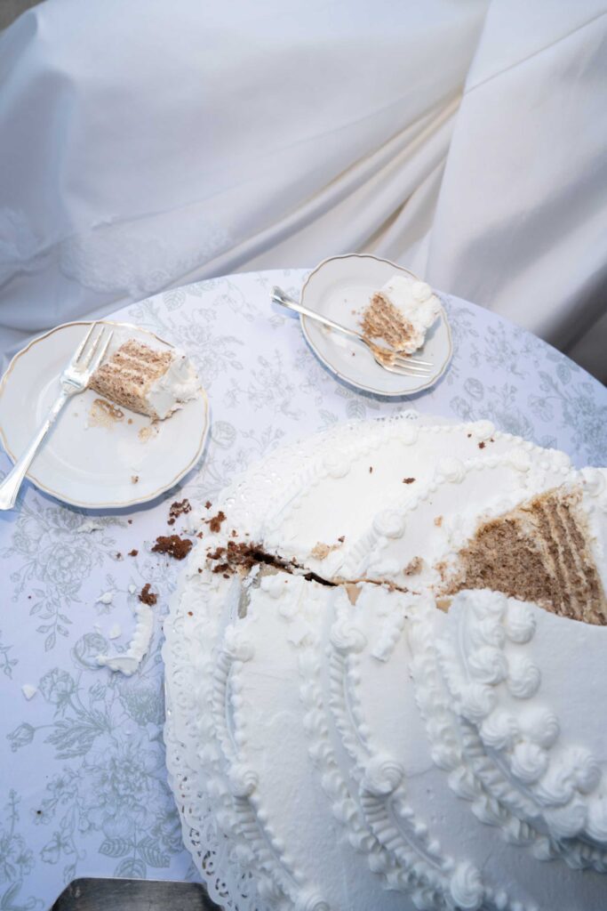Eine mit Zuckerguss verzierte Torte und Tortenstücke auf einer geblümten Tischdecke bei einer Hochzeit im Rosewood Schloss Fuschl.