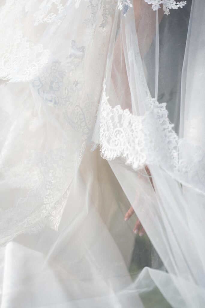 Eine Hand, die durch einen zarten, mit Spitze besetzten Brautschleier bei einer Hochzeit im Rosewood Schloss Fuschl zu sehen ist.
