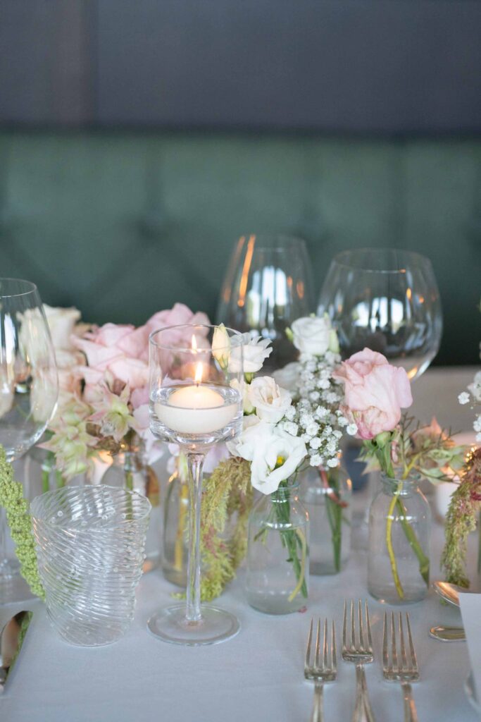 Tischdekoration mit Blumenvasen und einer Schwimmkerze bei einer Hochzeit im Rosewood Schloss Fuschl.