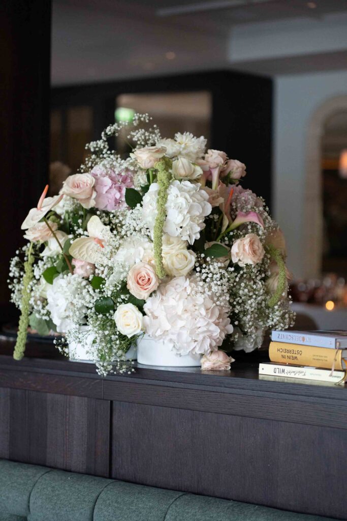 Großes Blumenarrangement aus weißen und zartrosa Blüten neben Büchern bei einer Hochzeit auf Schloss Fuschl.