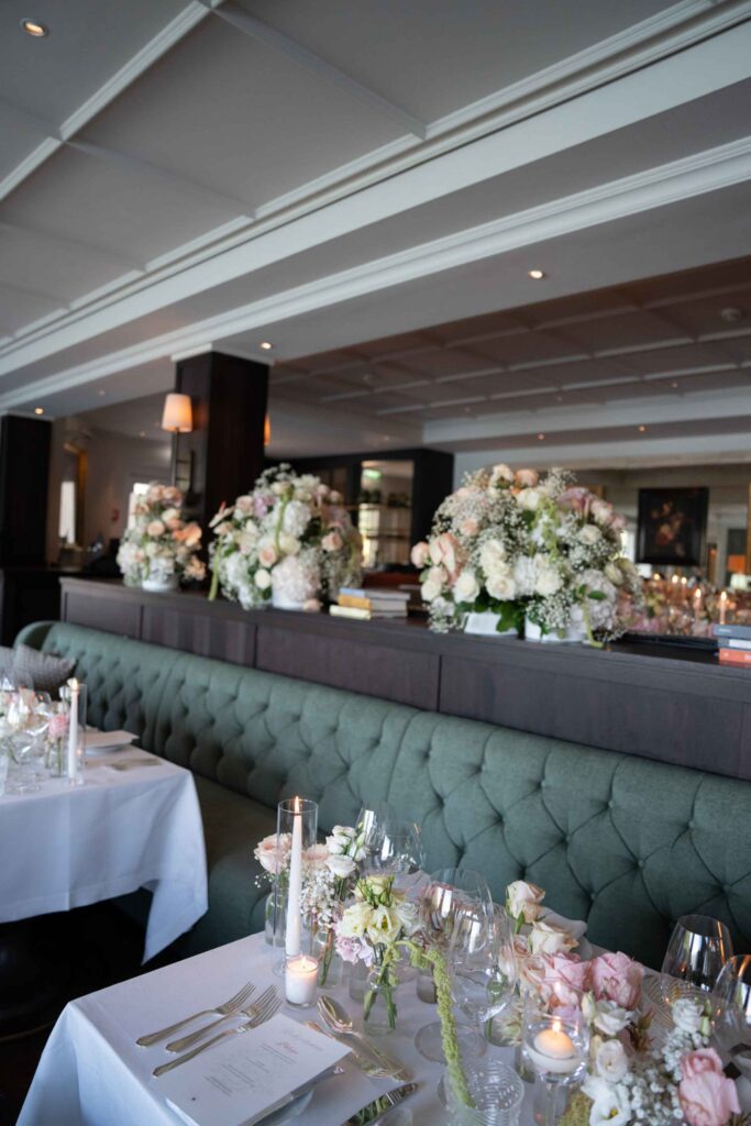 Restaurantbereich mit grünen Sitznischen und Blumengestecken als Tischdekoration für eine Hochzeit im Schloss Fuschl.