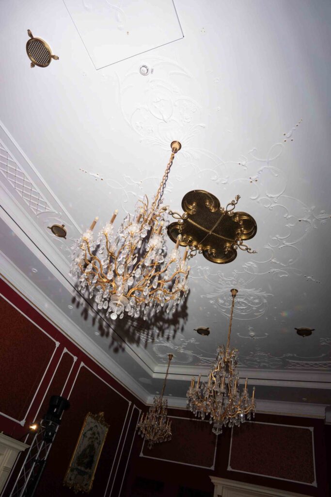 Im Rosewood Schloss Fuschl hängen drei Kristallkronleuchter von einer kunstvoll verzierten, weißen Decke herab.