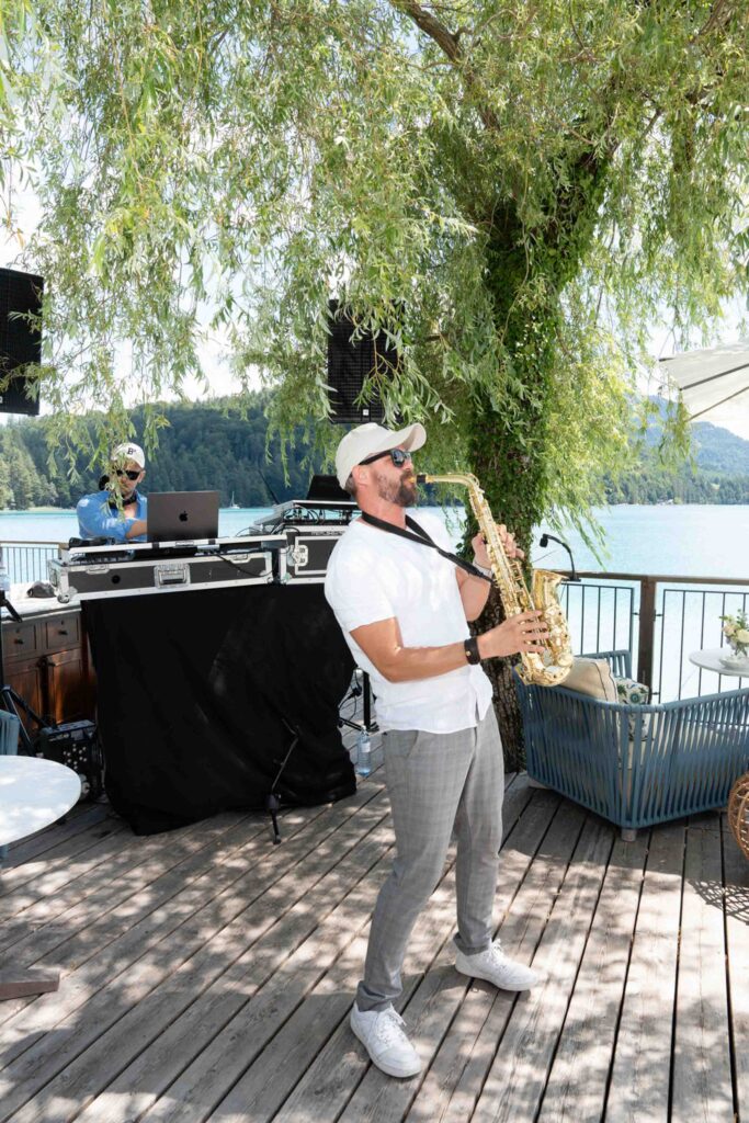 Bei einer Hochzeit am See im Rosewood Schloss Fuschl spielt ein Mann neben einem DJ Saxophon.