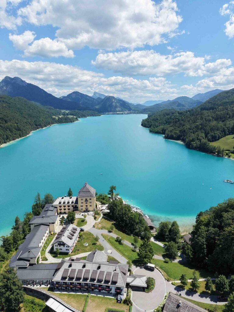 Luftaufnahme des Rosewood Schloss Fuschl, eines Hotelkomplexes auf einer Halbinsel an einem türkisfarbenen See.