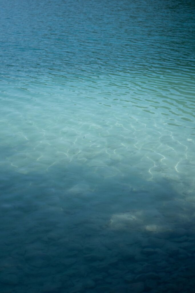 Klares, plätscherndes türkisfarbenes Wasser über einem felsigen Seegrund im Rosewood Schloss Fuschl.